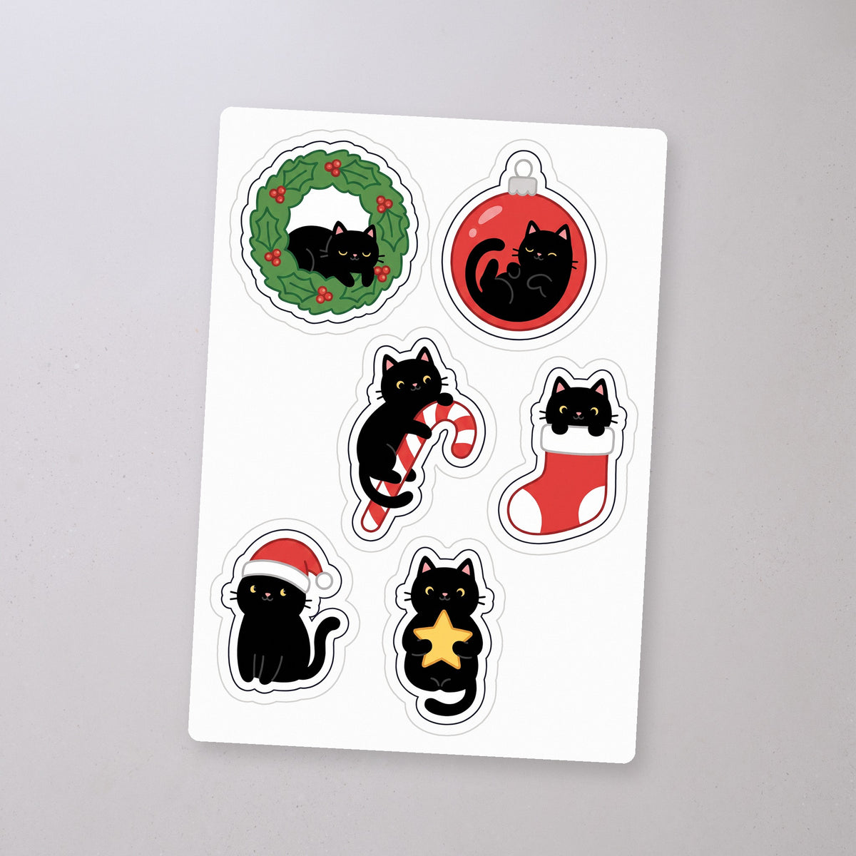 Black Cat Christmas Ornaments Sticker Sheet, sticker sheet on a concrete floor