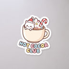 Hot Cocoa Club Cat Sticker on a concrete floor