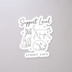 Support Local Street Cats Line Art Sticker on a concrete floor